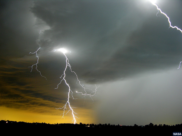 A thunderstorm cloud viewed from the ground with spectacular lightning strikes next to a thick rain shaft.  The sun angle makes the background color a brilliant golden yellow.  Nitrogen oxide molecules are indicated near the lightning strike.